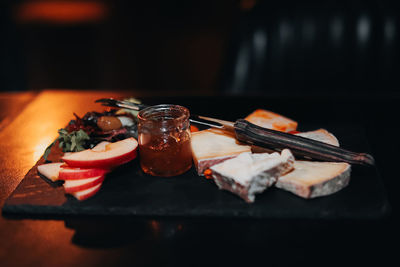 Composition of sliced cheese, a jar of honey and pieces of apples on a wooden stand