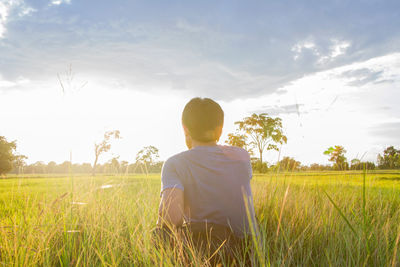 Rear view of man sitting on field against sky