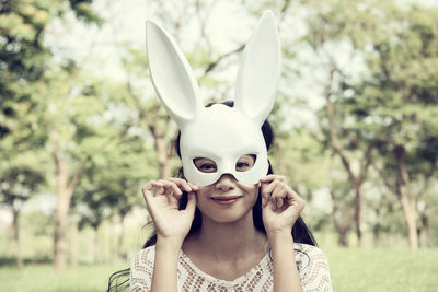 Portrait of young woman wearing mask while standing against trees at park