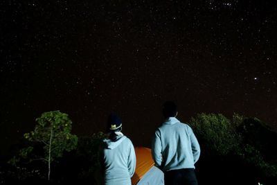 Rear view of friends looking at star field against sky during night