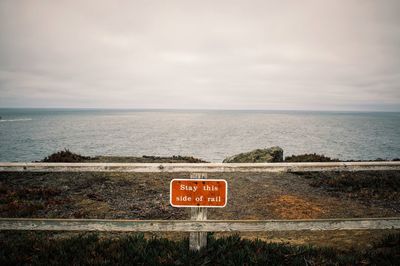 Information sign by sea against sky