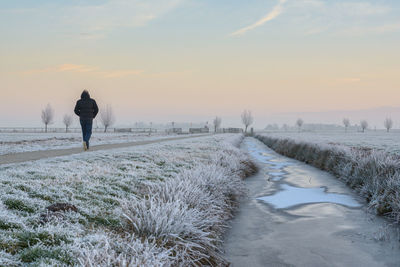 Rear view of man walking on snow covered landscape against sky