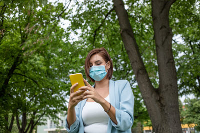Smiling woman wearing mask using smart phone outdoors