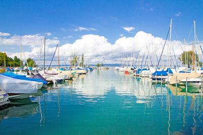 Sailboats moored at harbor against blue sky