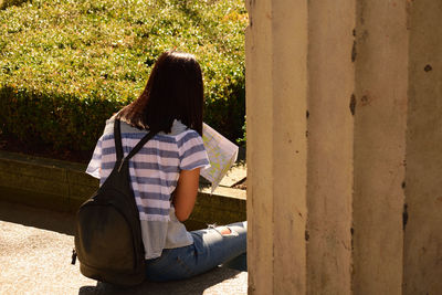 Rear view of woman with backpack and map sitting outdoors