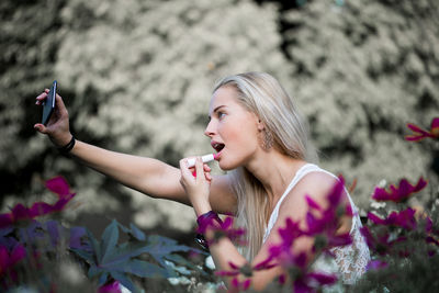 Side view of young woman applying lipstick at park