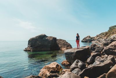 Man standing on rock by sea against sky