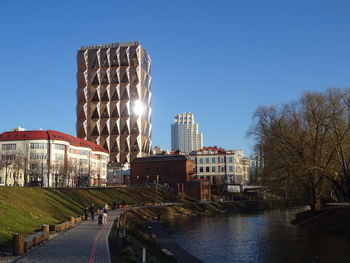 Buildings by canal against clear blue sky