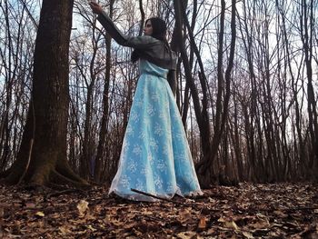 Woman standing by bare tree in forest