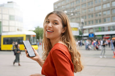 Portrait of woman walking in berlin alexanderplatz holding a mobile phone with city background