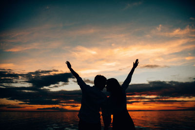 Silhouette women standing by sea against sky during sunset