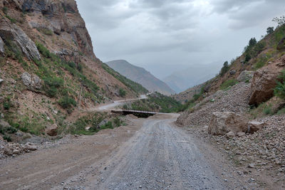 Dirt road by mountains against sky