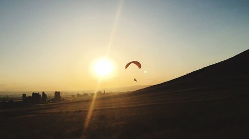 Person pagragliding over field against sky during sunset