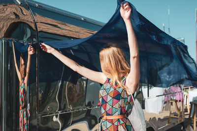 Woman holding blue scarf standing against bus