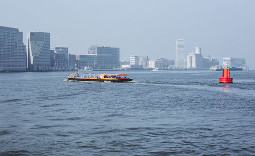 Ship sailing on sea against buildings in city