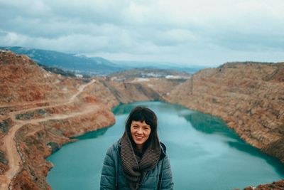 Portrait of smiling young woman in mountains against sky