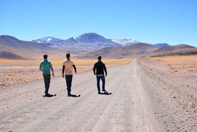 Rear view of people walking on desert against clear sky