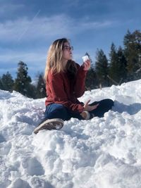 Woman sitting on snow against sky