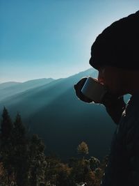 Man drinking coffee on mountain against sky