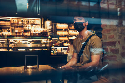 Young man sitting in coffee shop at store front in the city center in the evening