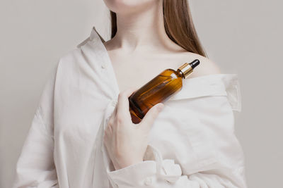 Midsection of woman holding bottle against white background