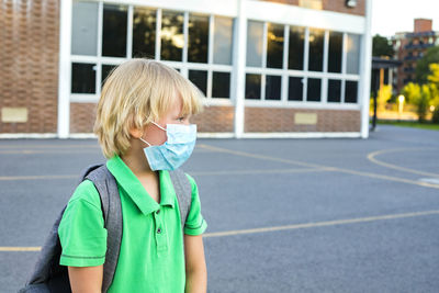 Child in face mask during corona virus outbreak, standing near school.