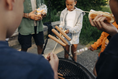 Boy roasting sausages with friends at summer camp
