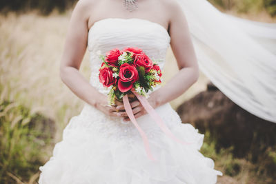 Midsection of bride holding rose bouquet while standing on field