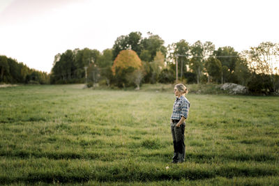 Female farmer with hands in pockets standing on field during sunset