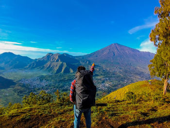 Rear view of man standing on mountain against sky