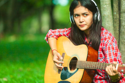 Young woman playing guitar while sitting at park