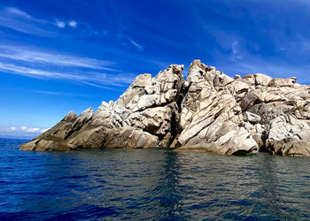 Rock formation by sea against blue sky