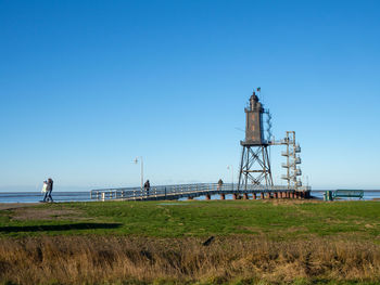 Lighthouse on field against clear blue sky