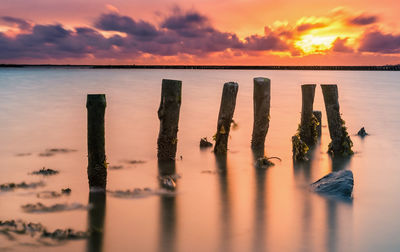 Wooden posts in sea against sky during sunset