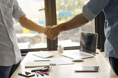 Midsection of business colleagues shaking hands in office