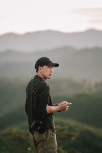 Side view of young man standing against sky