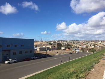 Cars on road by buildings in city against sky