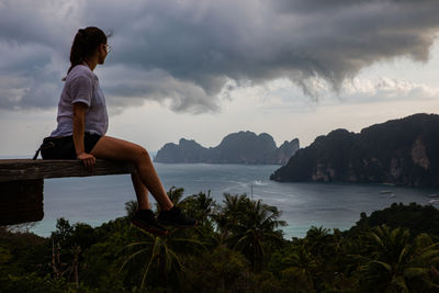 Side view of woman sitting at observation point against sea