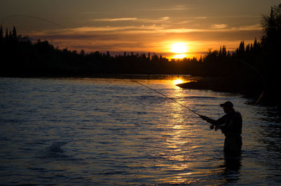 Silhouette man fishing in lake against sky during sunset