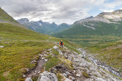 Rear view of hiker climbing on mountain against cloudy sky