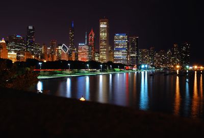 Illuminated buildings by river against sky at night