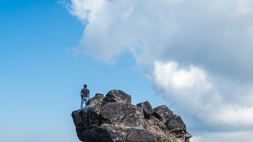 Low angle view of man standing on rock against sky