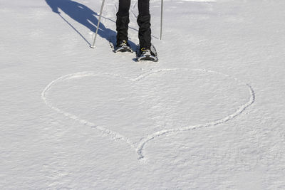 Low section of person standing by heart shape on snowy land