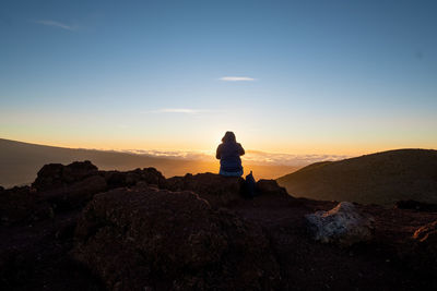 Rear view of man looking at rock against sky during sunset