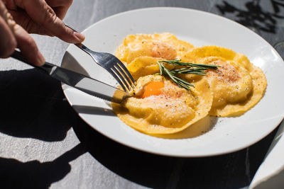 Cropped image of person having fried egg in plate on table