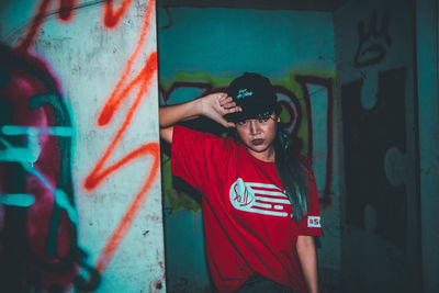 Young woman wearing sunglasses standing against graffiti wall