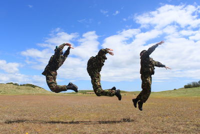 Full length of soldiers in mid-air over field against sky