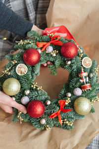 Woman pulls out a beautifully decorated christmas wreath with red ornaments from wrapping paper.