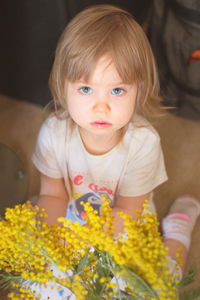 High angle portrait of cute baby girl with yellow flowers sitting at home