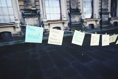 Paper with text hanging on clothesline at footpath